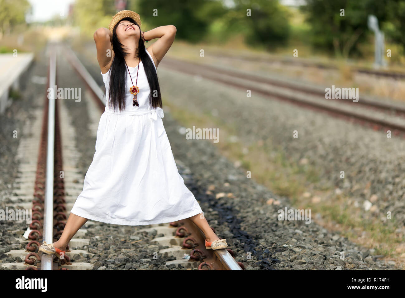 Young woman standing and relaxing on a rural railway track in a white dress on a summer evening Stock Photo