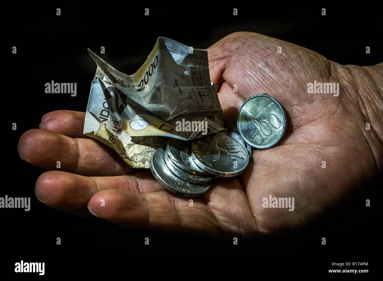 Indonesia rupiah small bill and coins in the hand of an asian person isolated. Concept of begging for leaving, poor person. Stock Photo