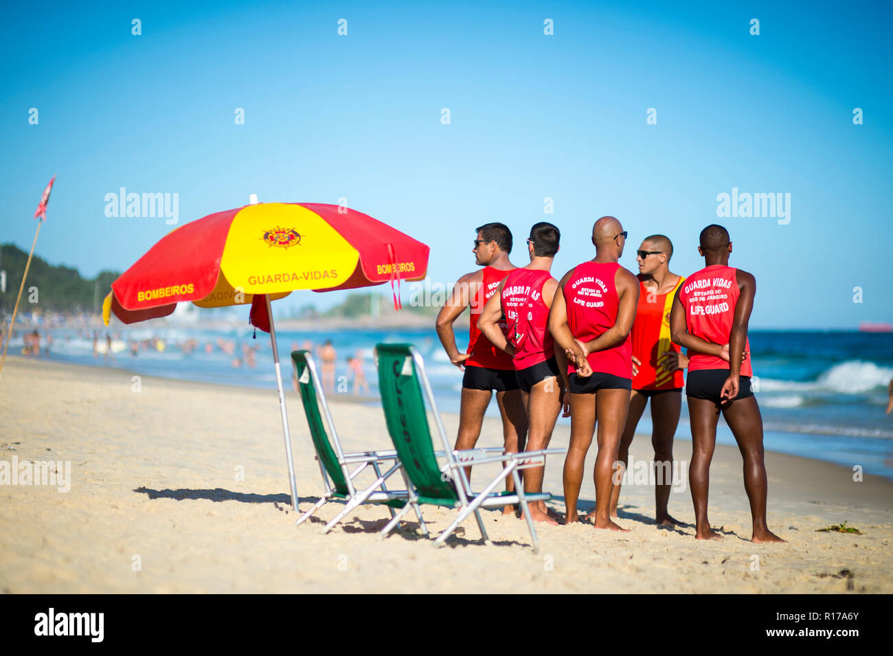 RIO DE JANEIRO - CIRCA FEBRUARY, 2018: A group of lifeguards stand together in uniform on Ipanema Beach next to an umbrella Stock Photo