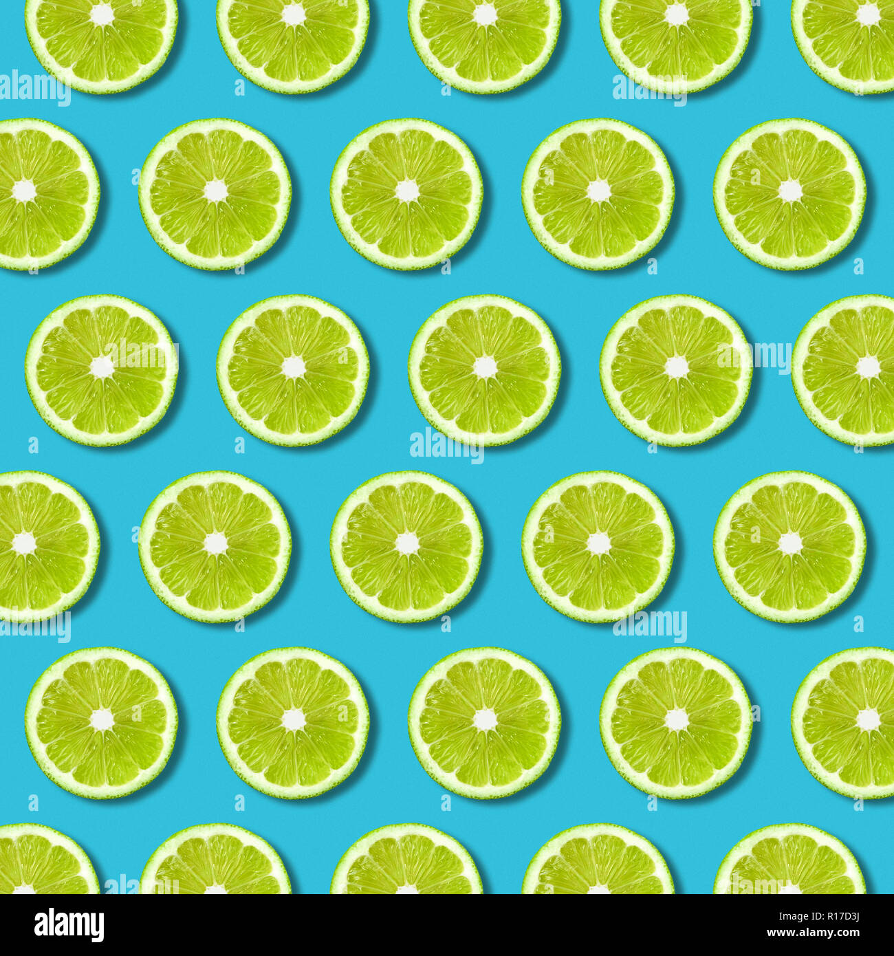 Green lime slices pattern on vibrant turquoise color background. Minimal flat lay food texture Stock Photo