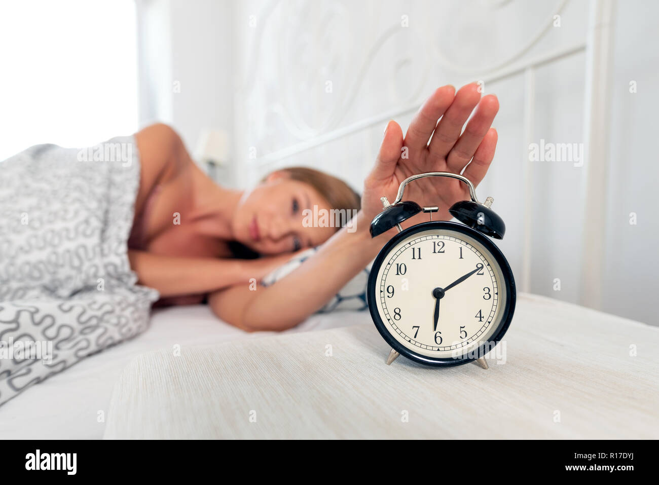 Woman hand turns off the alarm clock waking up at morning Stock Photo