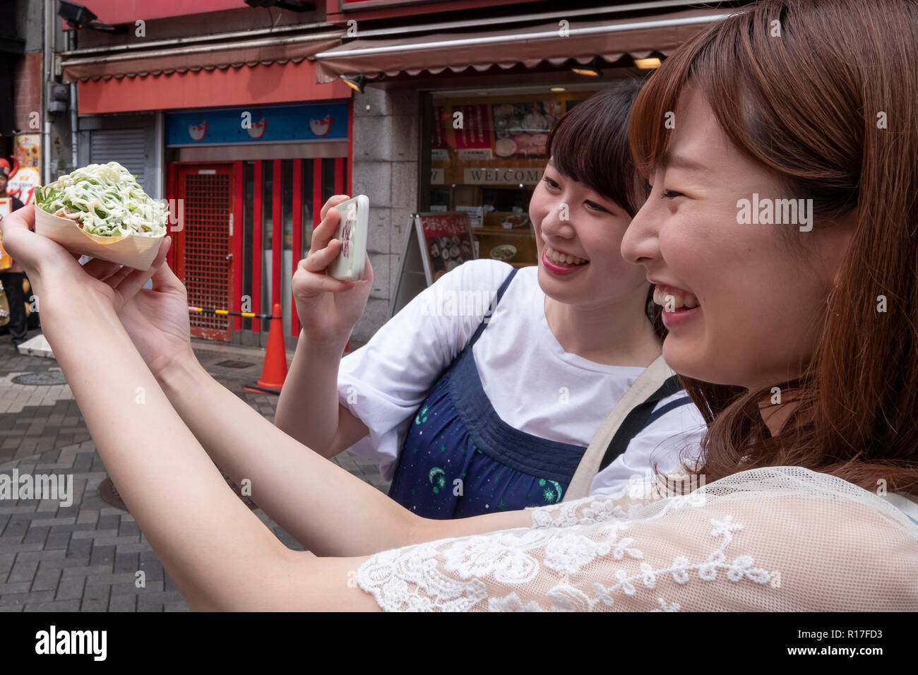 Young Japanese women photograph their food in Dotonbori, Osaka, Japan Stock Photo