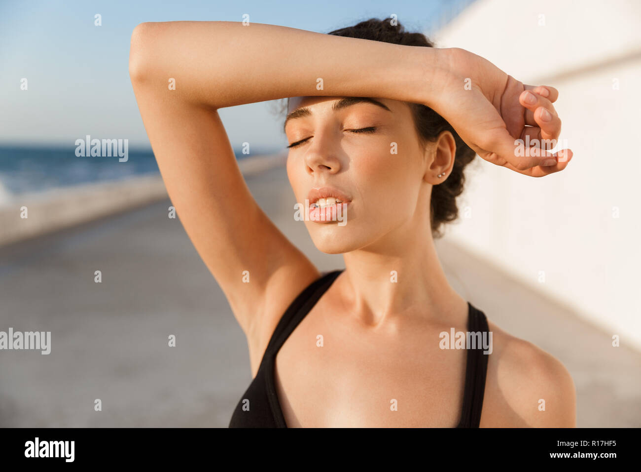 Tired young sportswoman standing outdoors, wiping forehead with hand Stock Photo