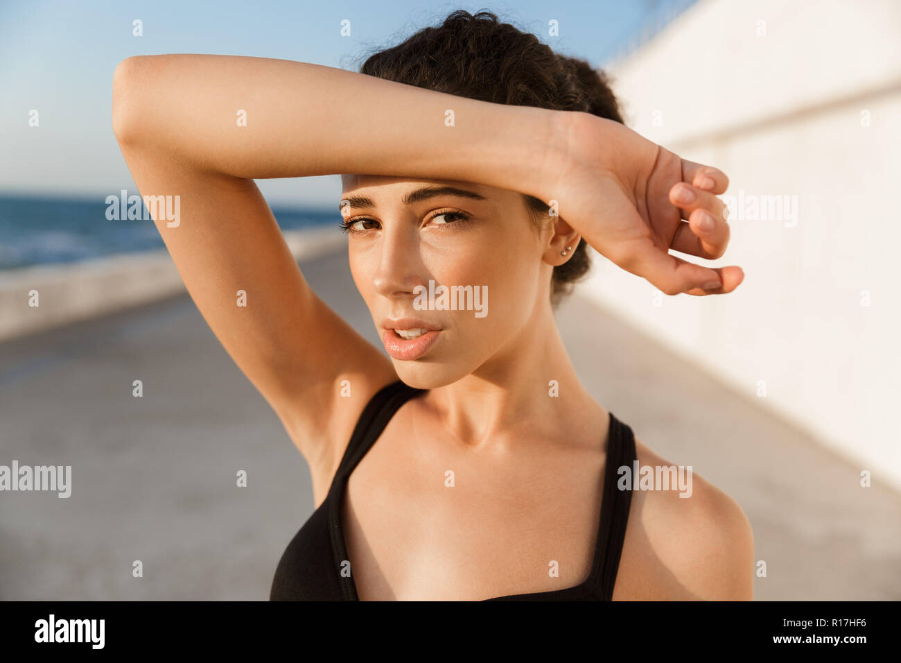 Exhausted young sportswoman standing outdoors, wiping forehead with hand Stock Photo