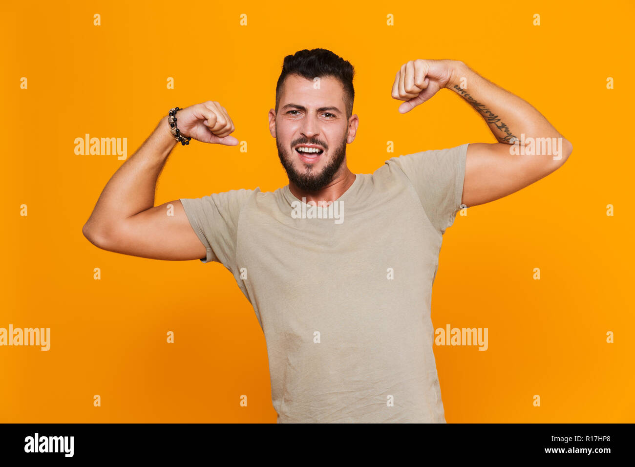 Portrait of a strong young casual man standing isolated over orange background, flexing biceps Stock Photo