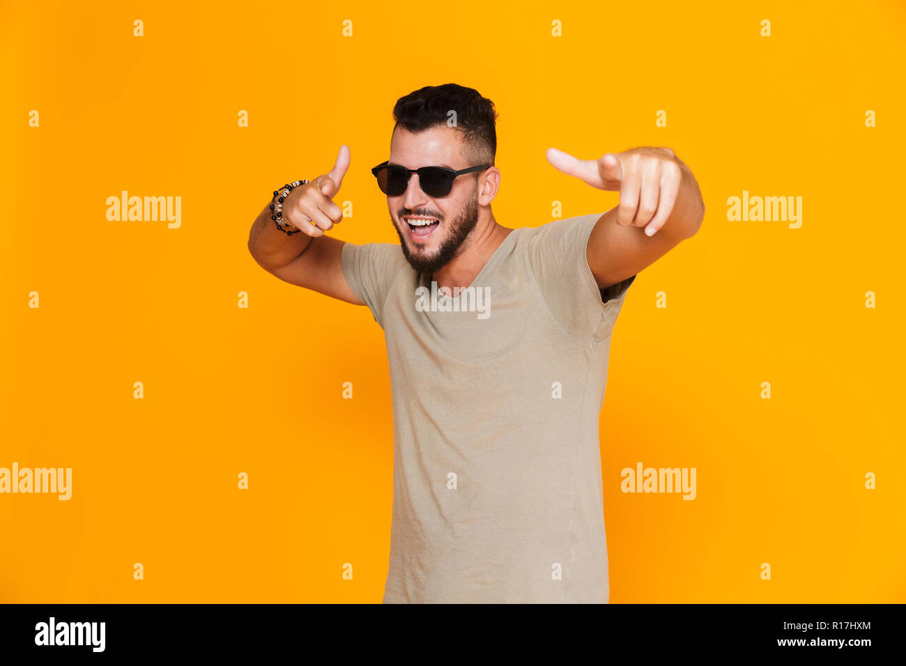 Portrait of a cheerful young casual man in sunglasses standing isolated ...
