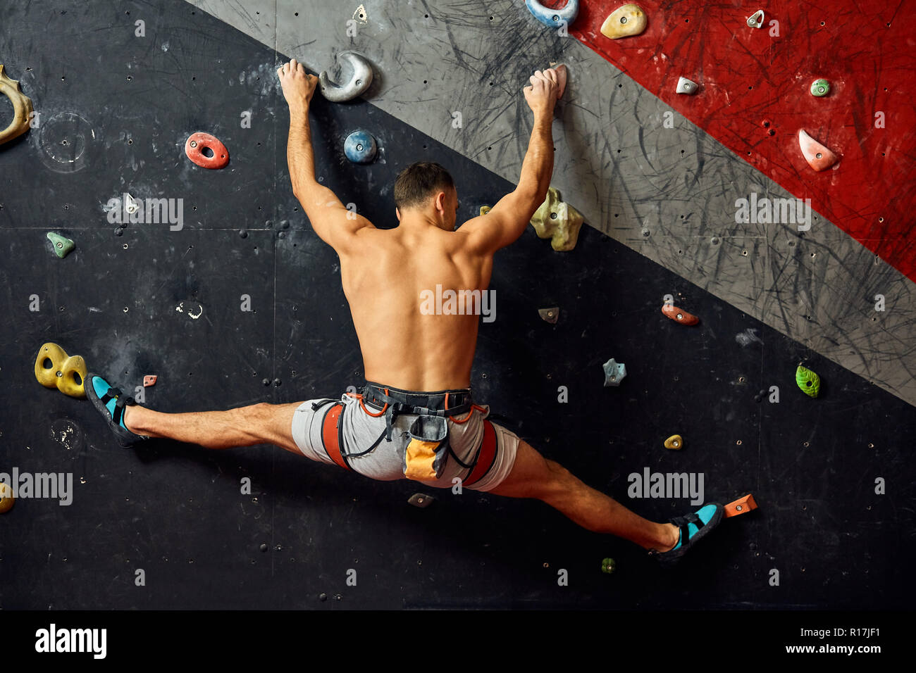 Young man climbing on artificial rock, hanging on safety ropes Stock