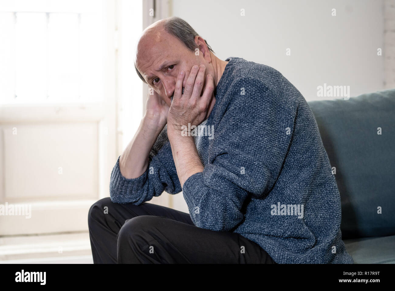 Overwhelmed old senior man suffering alone at home feeling confused sad alone on couch at home in Aging Retirement widower Dementia and Alzheimer conc Stock Photo