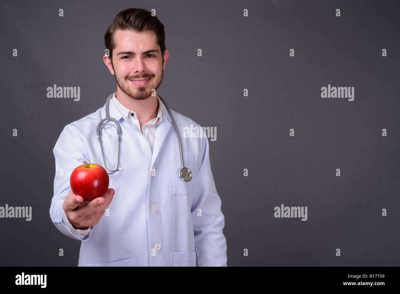 Young handsome bearded man doctor against gray background Stock Photo