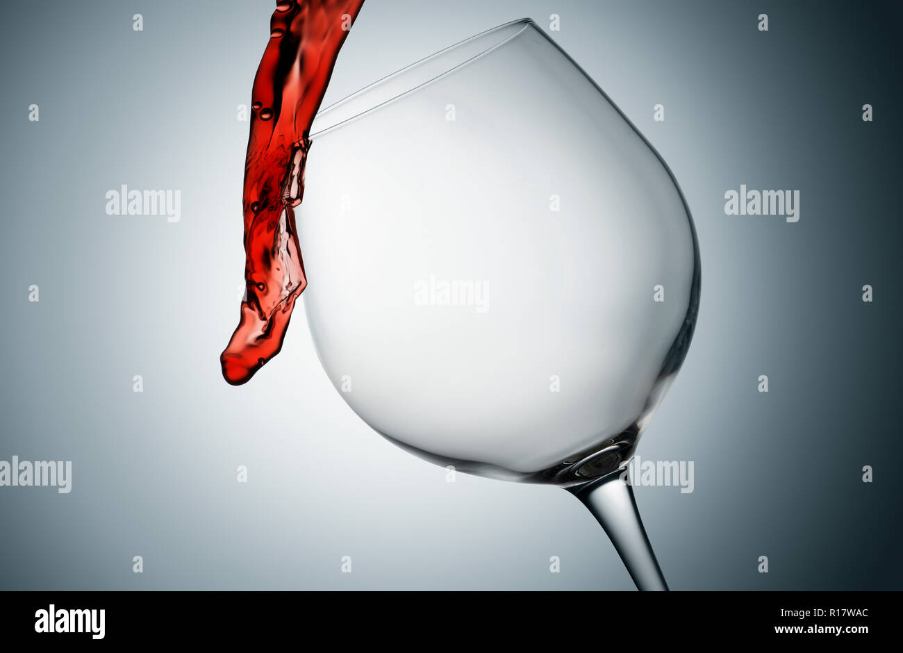 Pouring and spilling red wine out of tilted glass, plain background Stock Photo