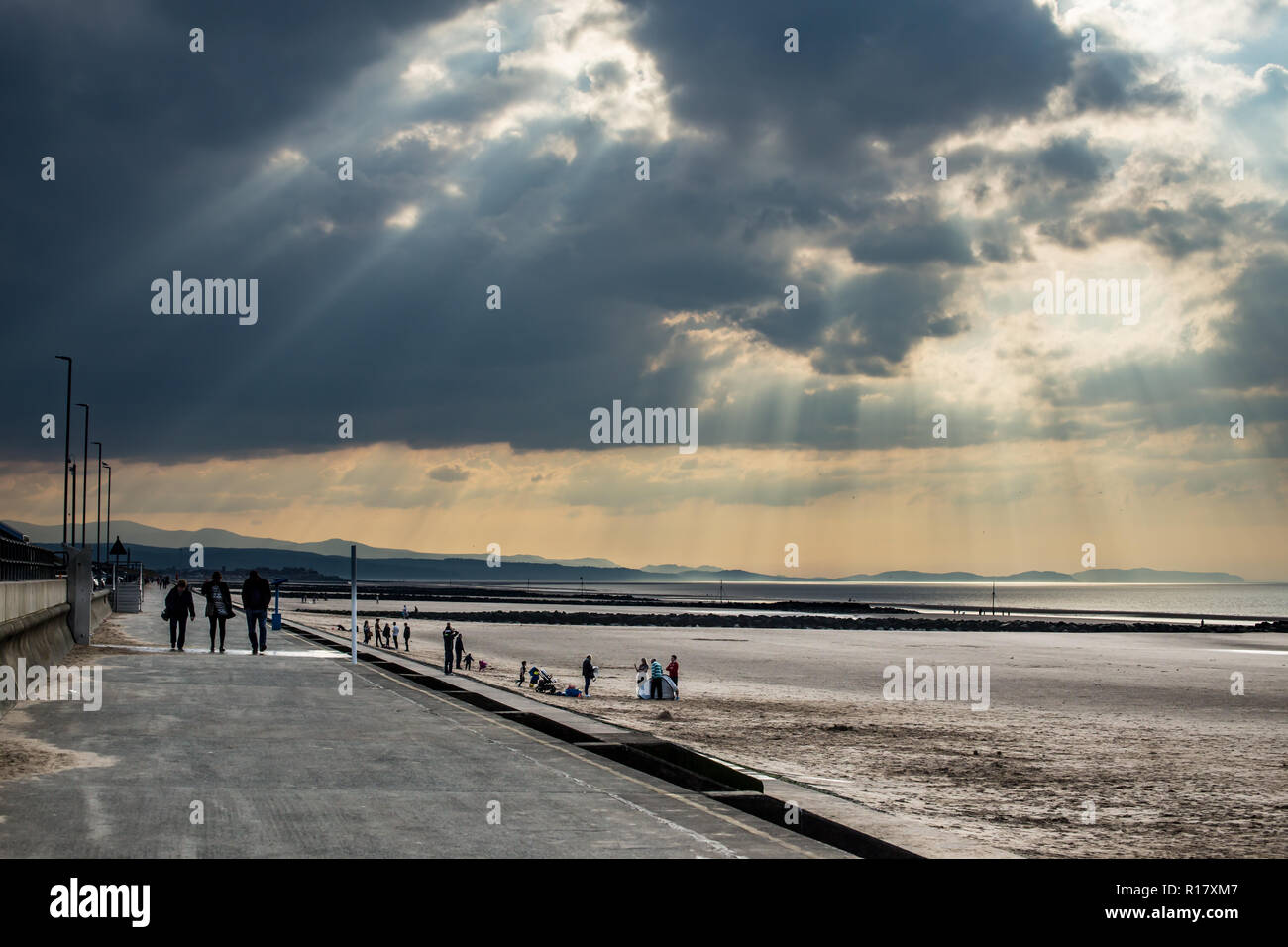 Empty beach on a gloomy moody day with sun beams coming through the stormy clouds.  Towyn town and the mountains of Snowdonia are visible. Stock Photo