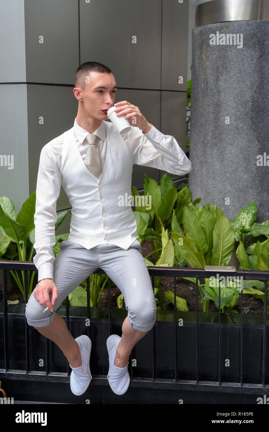 Young androgynous homosexual LGTB businessman drinking coffee and smoking cigarette Stock Photo