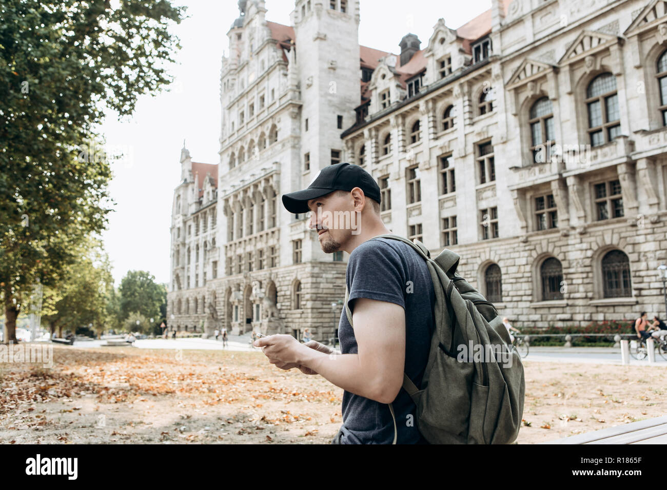 A tourist man or boy with a backpack or a student in Leipzig in Germany uses a mobile phone to view a map or call or for another. Stock Photo