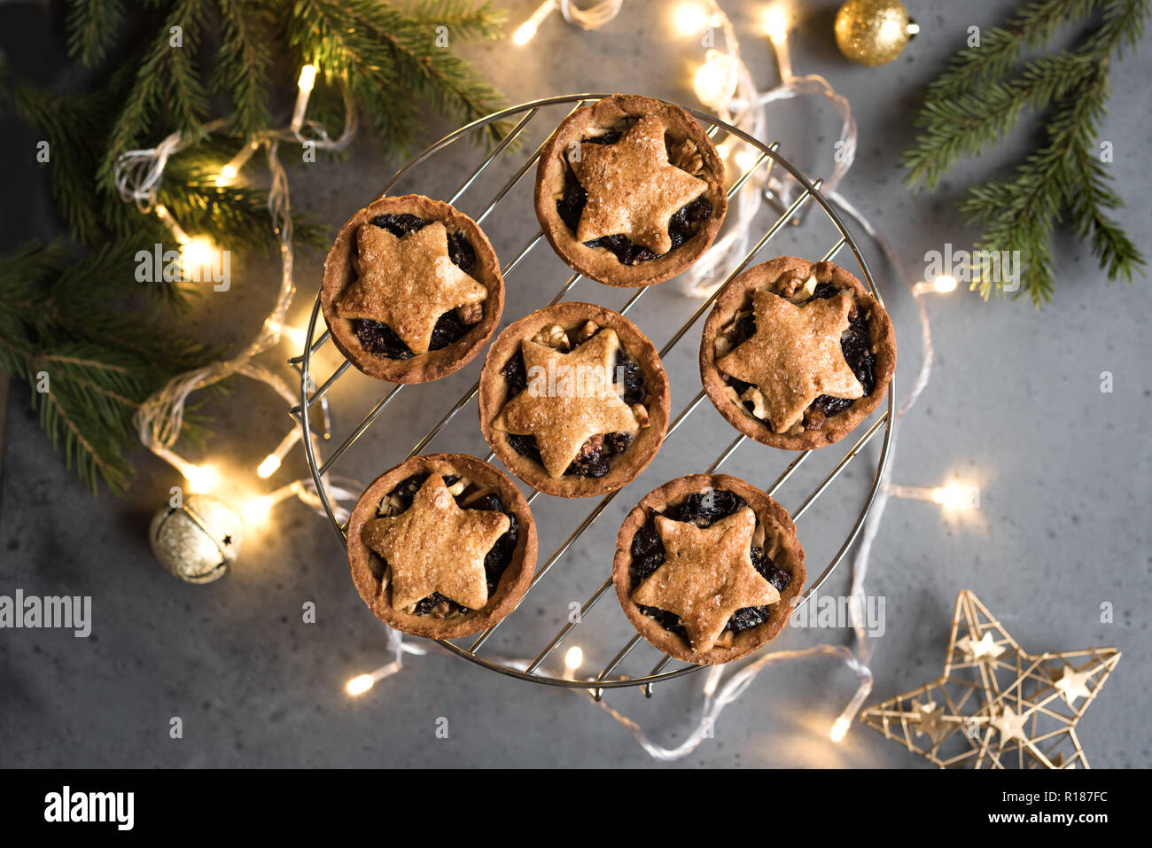 Mince Pies for Christmas on grey background with light and festive decor. Traditional Christmas dessert - mince pies with fruits and nuts. Stock Photo