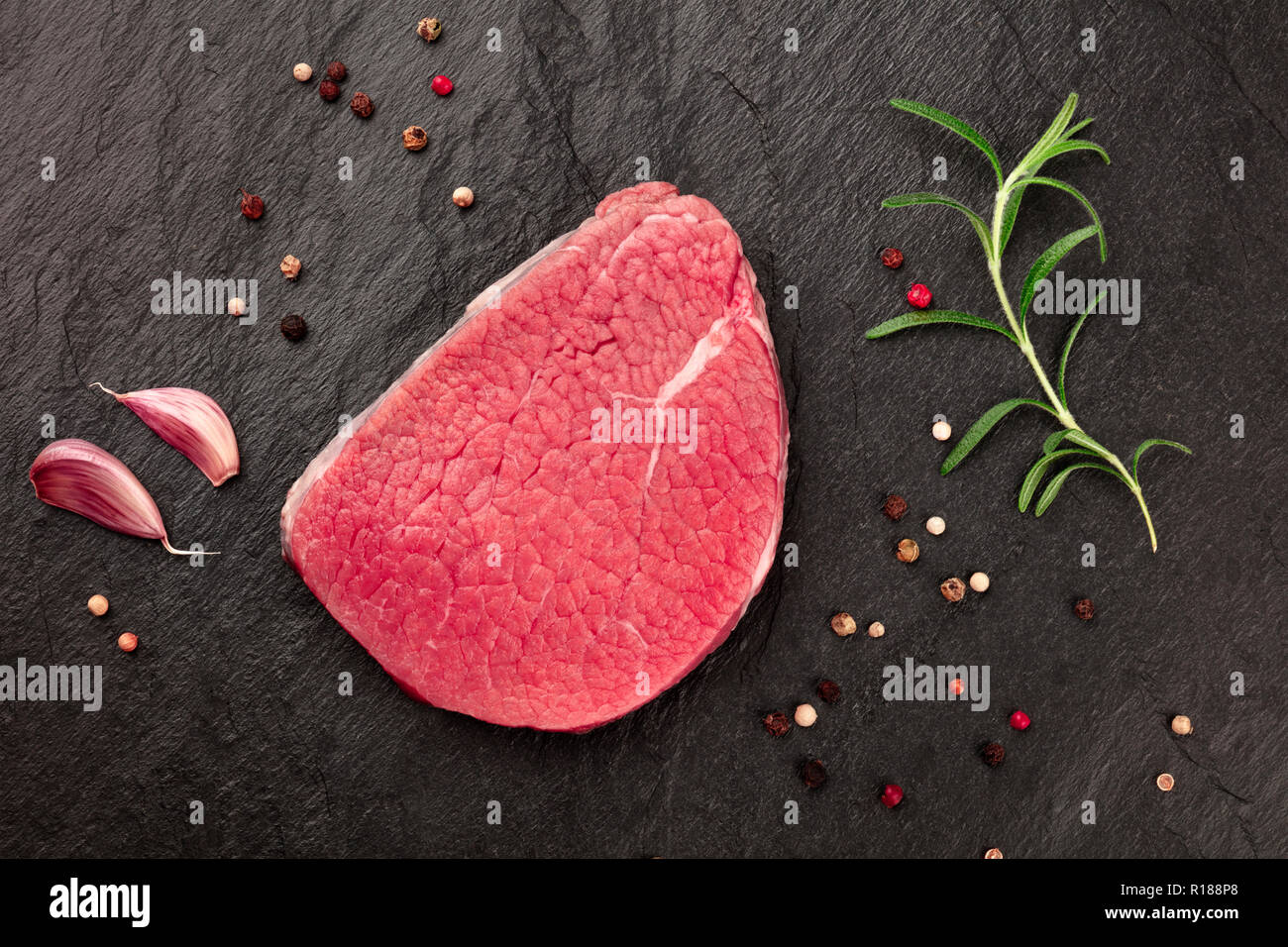 A photo of a steak of eye round beef, a raw cut, with rosemary, garlic, and pepper, shot from