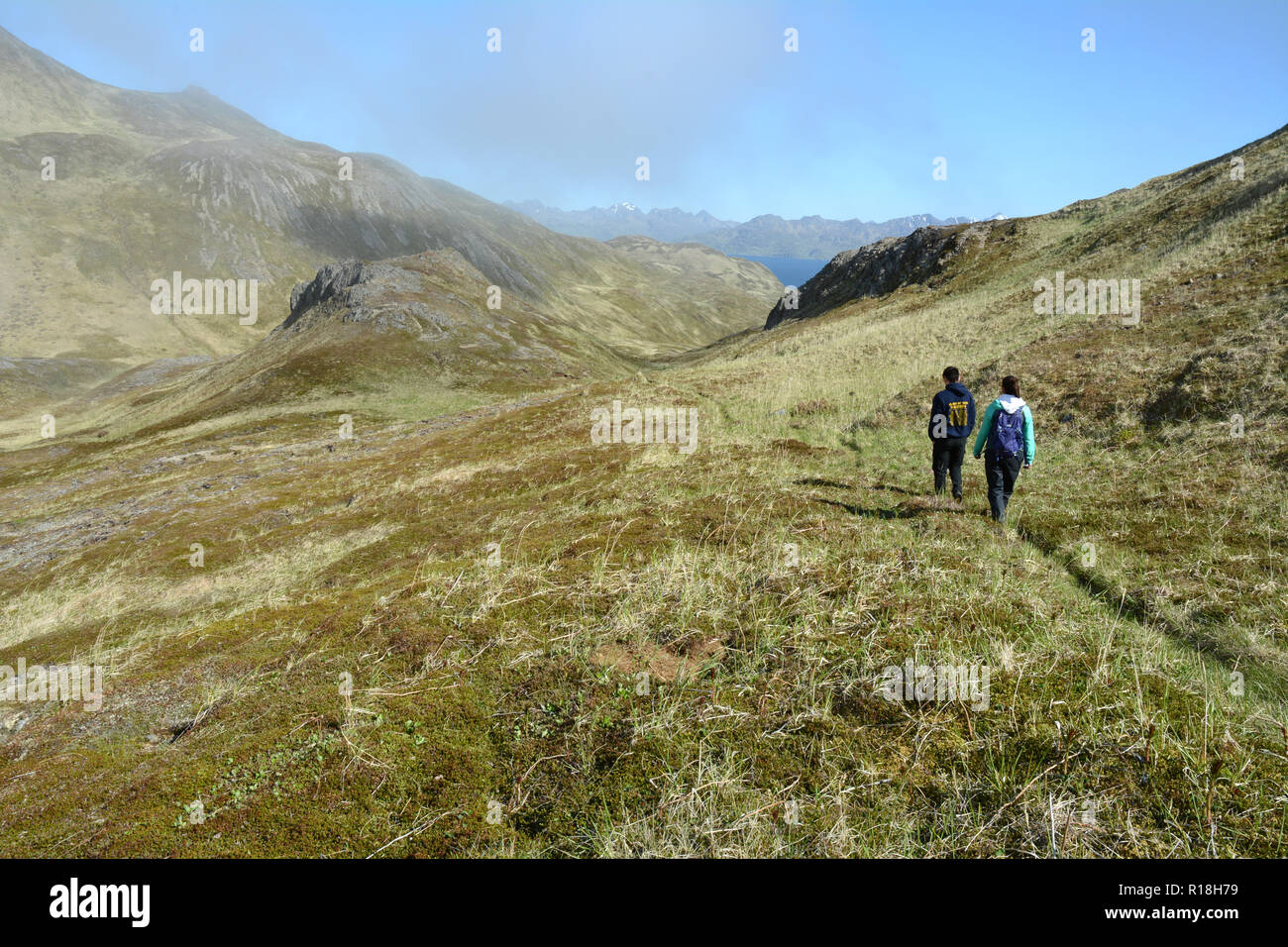 Two indigenous Unangan (Aleut) youth hiking along an ancient trail to the Pacific Ocean, in the Aleutian Islands, Unalaska, Alaska, United States. Stock Photo