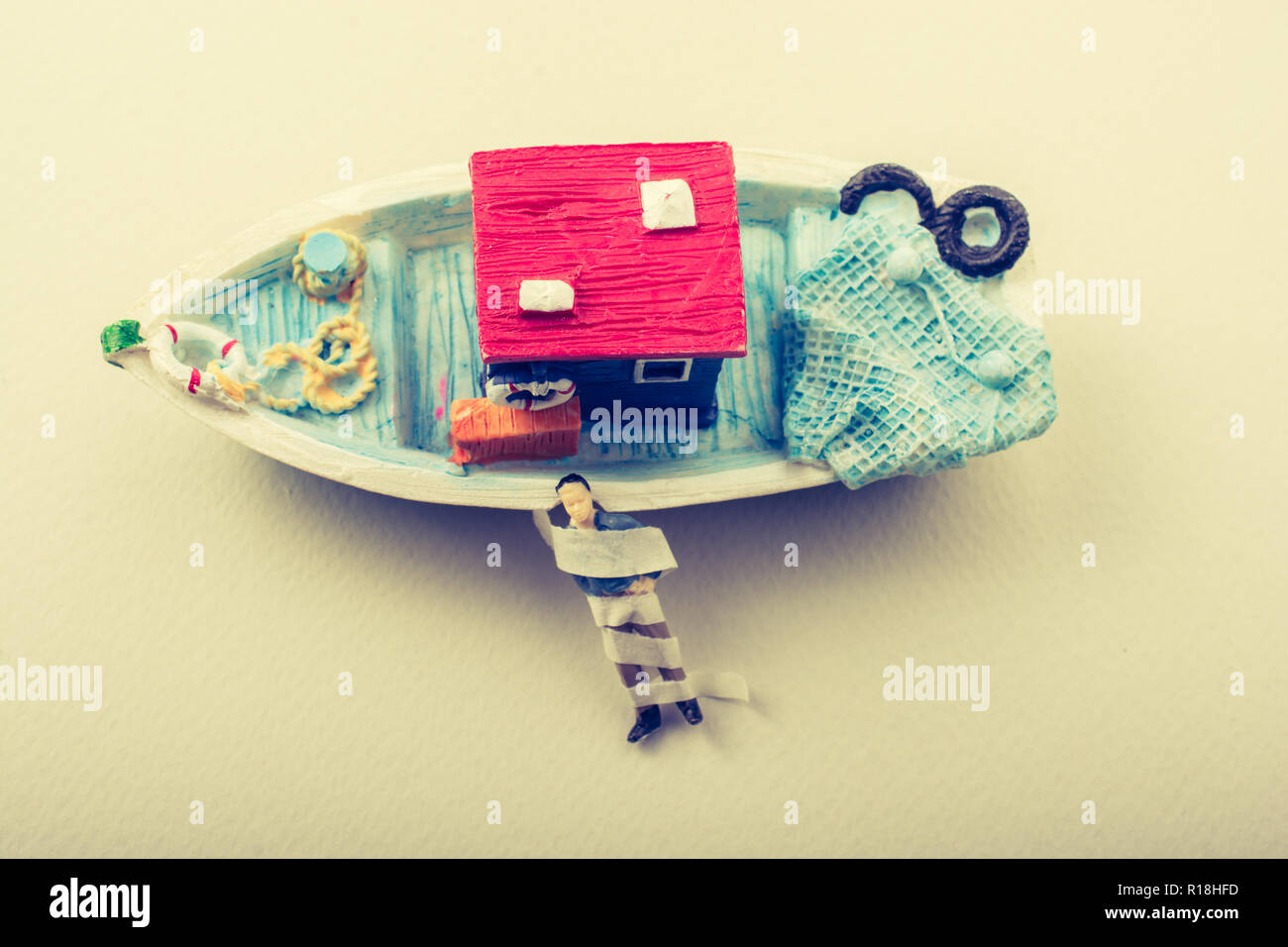 Tiny wrapped figurine of man model beside a model boat Stock Photo