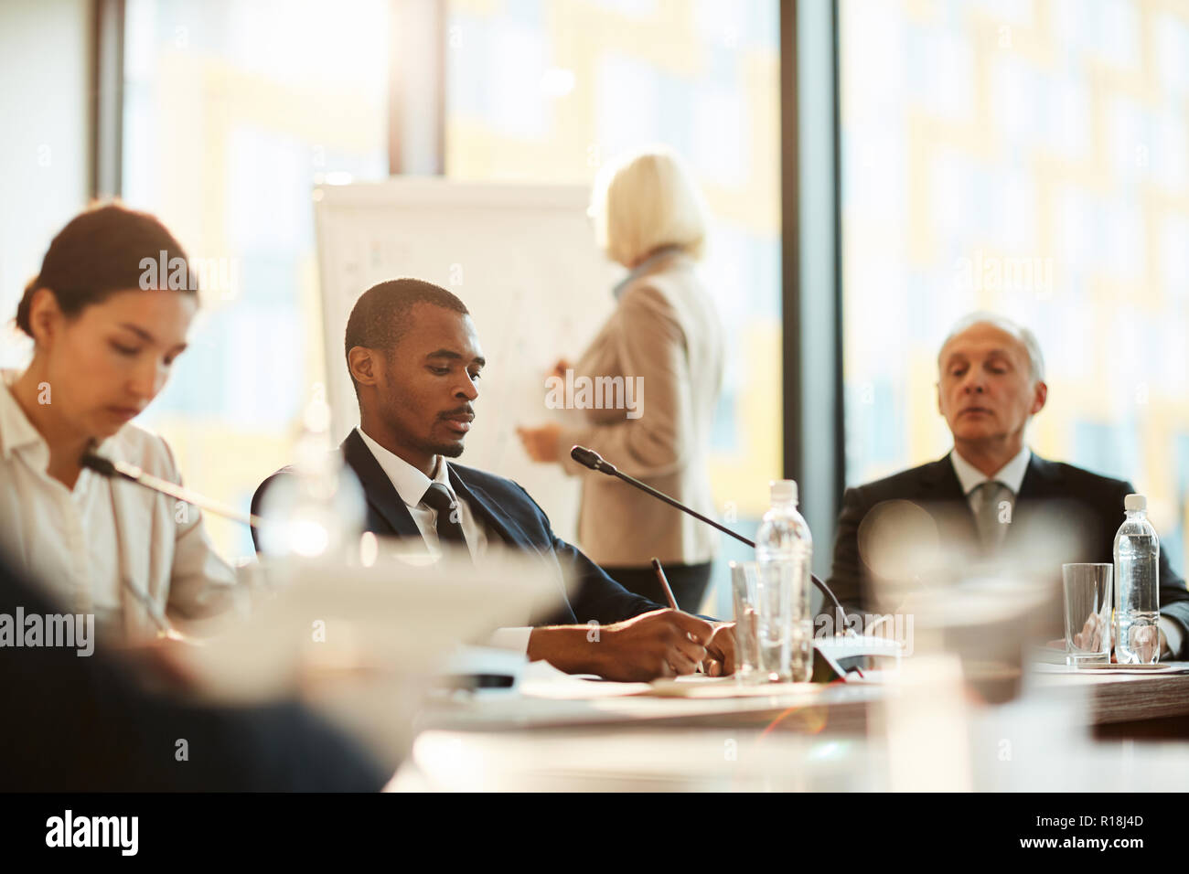African-american delegate making working notes while sitting at conference among colleagues Stock Photo