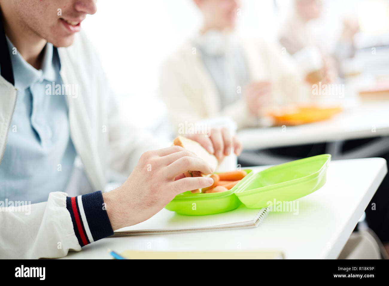 Contemporary student taking out sandwich from plastic container and going to eat it by desk Stock Photo