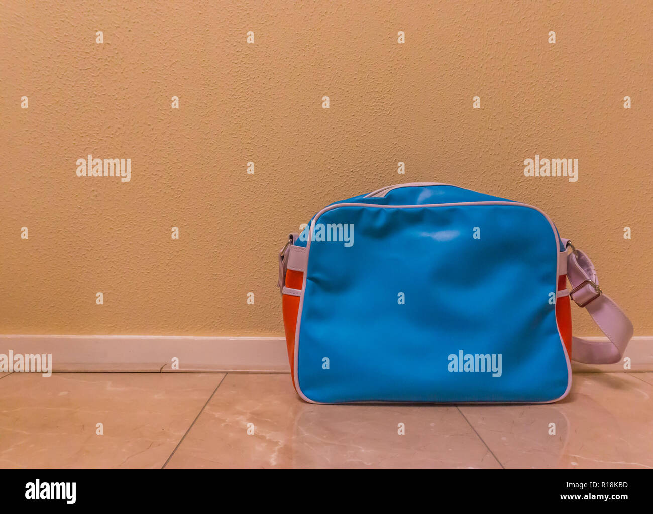 blue with red messenger school bag isolated in against a wall and standing on the floor in a room Stock Photo