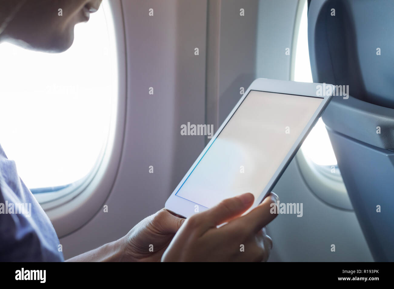 Passenger using tablet computer in airplane cabin during flight with wireless internet to read emails or an ebook, hands holding device with white emp Stock Photo