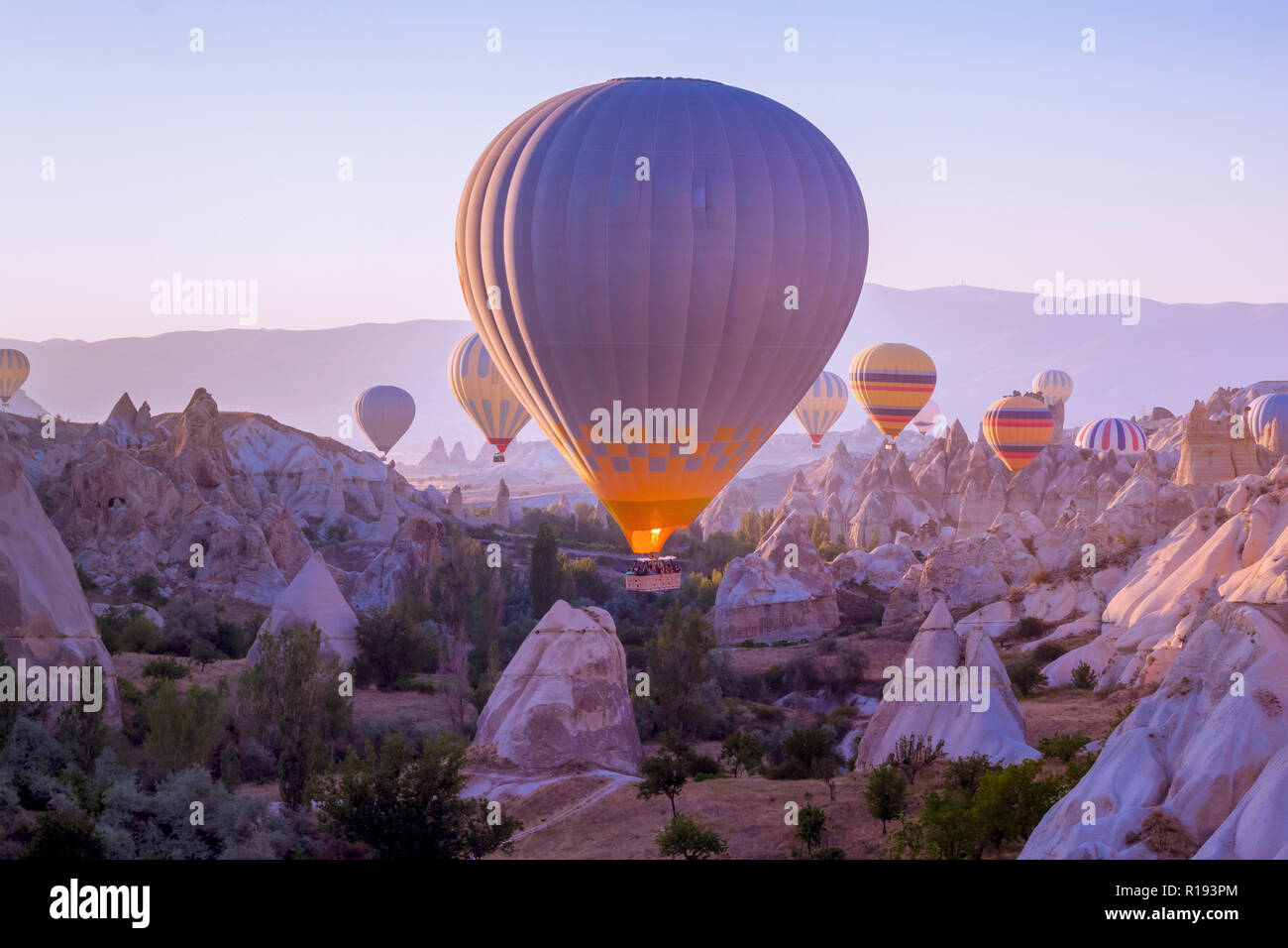 Hot air balloons flying in beautiful Cappadocia hilly landscape, amazing tourism attraction in Goreme, Anatolia, Turkey, morning sun light Stock Photo