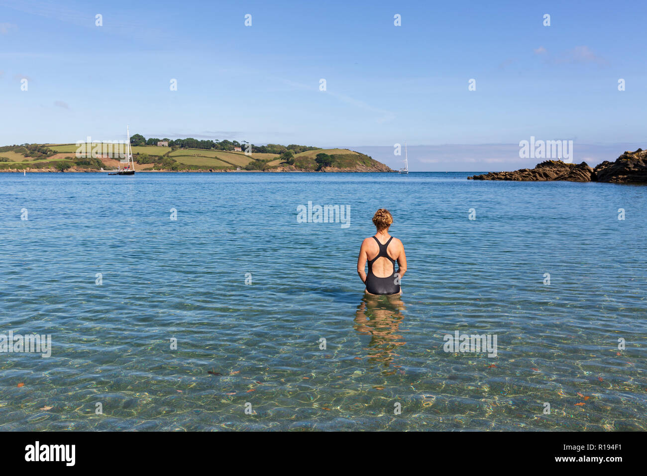 Woman wearing a swimming costume entering the cool, clear water at Bosahan Cove on the the Helford River Estuary in Cornwall, England. Stock Photo