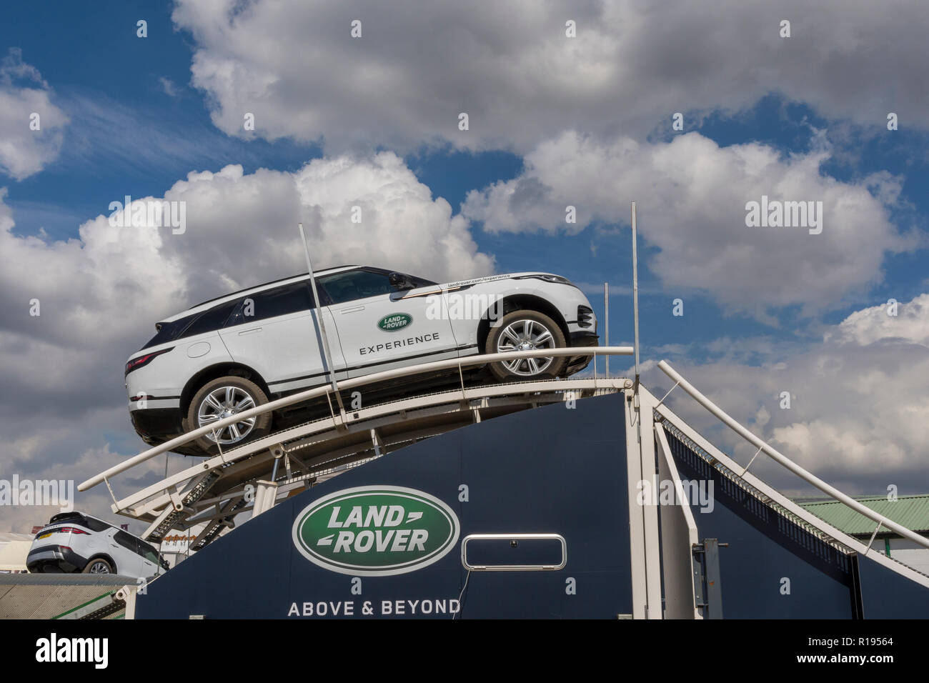 Land Rover Experience as the white vehicle climbs high on an hydrolic ramp against a blue sky background Stock Photo