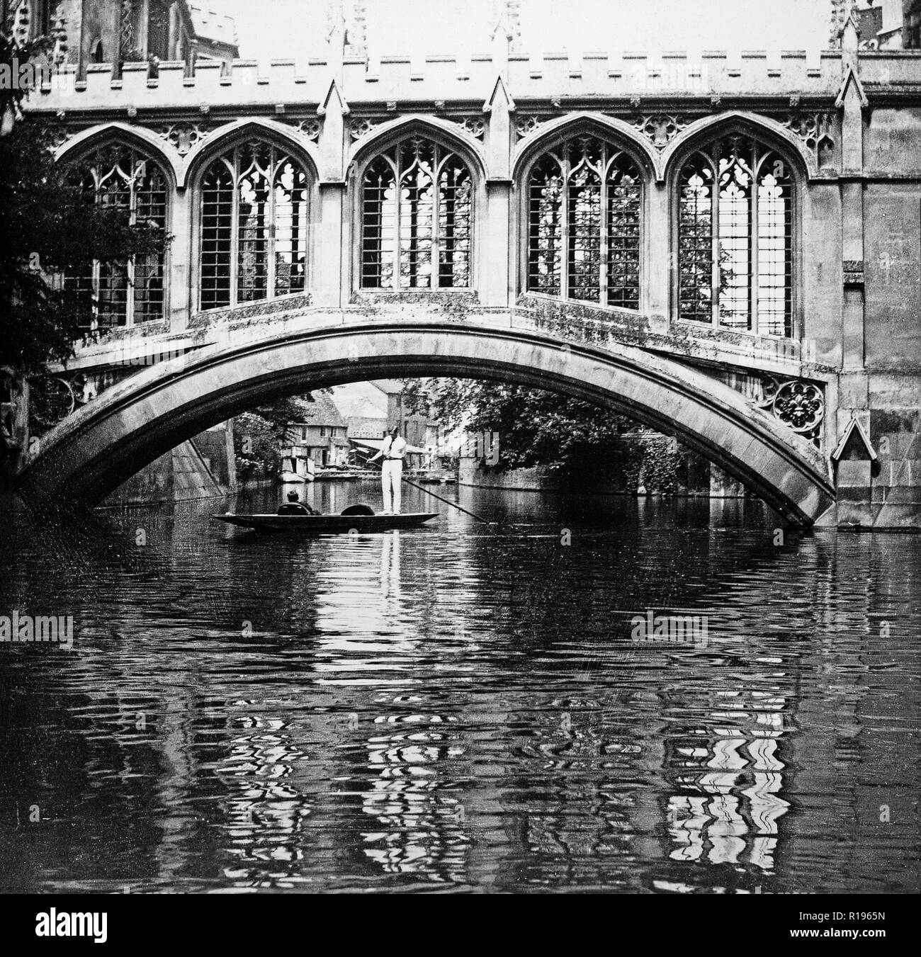 Black and white vintage photograph taken in 1924 showing the Bridge Of Sighs, a covered bridge at St.John's College, Cambridge, England. It was built in 1831 and crosses the River Cam between the college's Third Court and New Court. The architect was Henry Hutchinson. Photo shows a couple in punt, the traditional boat used on the river, with a man standing and using a pole. Stock Photo