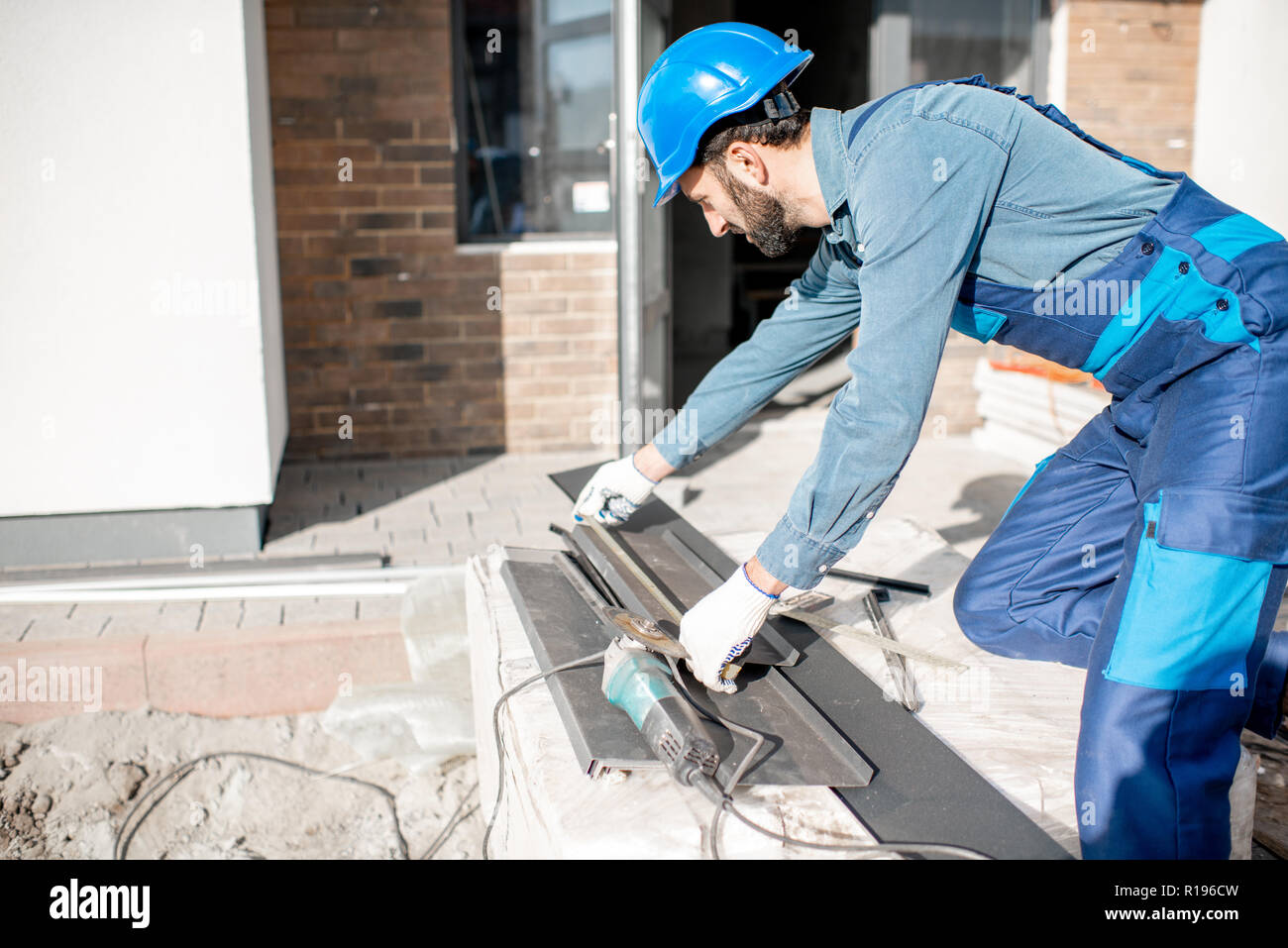 Builder in uniform measuring metal window sills for cutting on the construction site Stock Photo