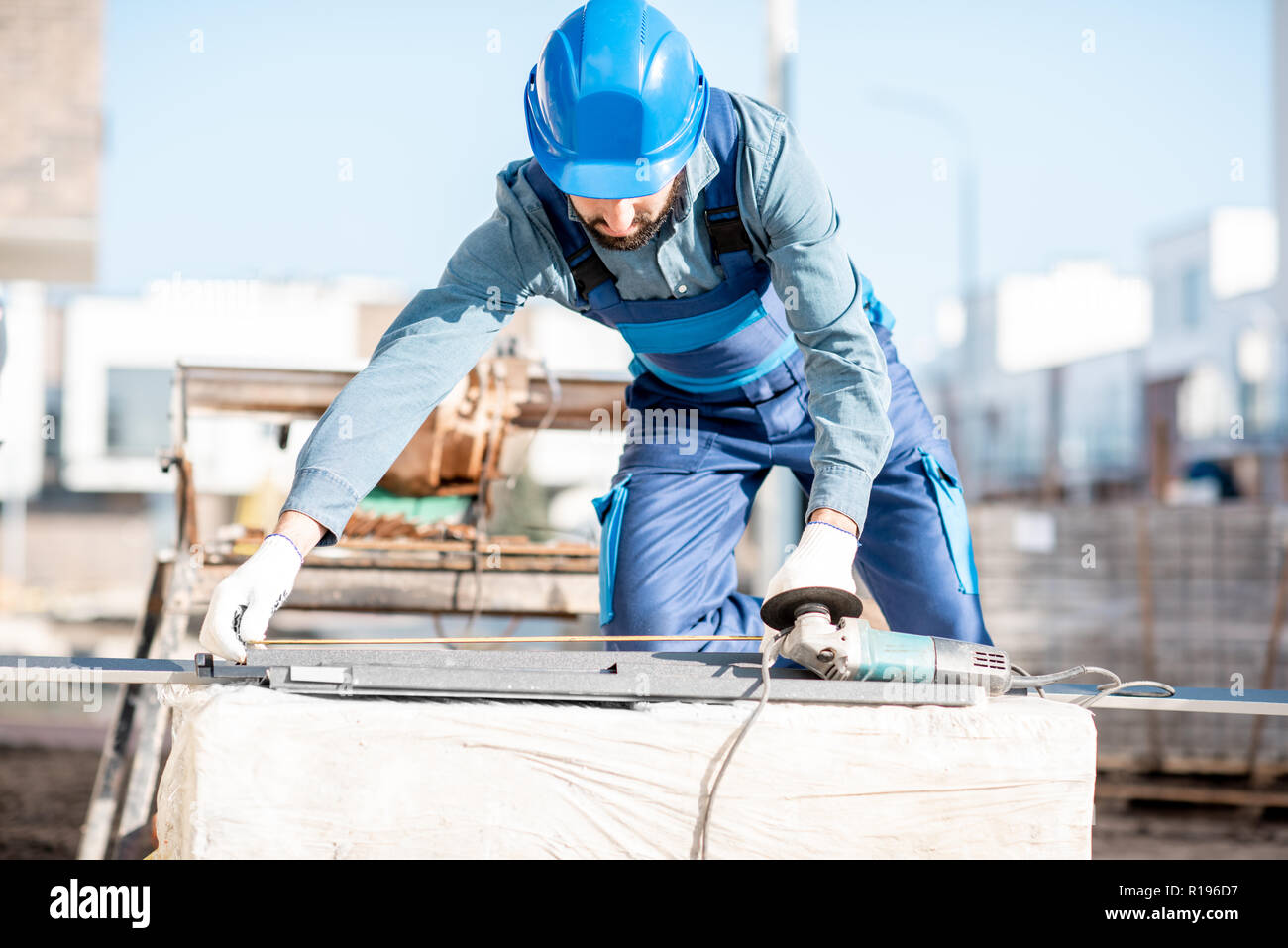 Builder in uniform measuring metal window sills for cutting on the construction site Stock Photo