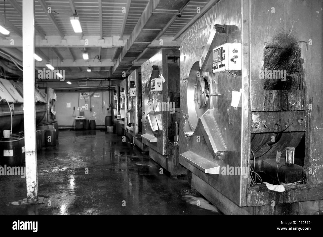 Black and white photo of the old workshop of washing with old washing machines and blue barrels of water Stock Photo