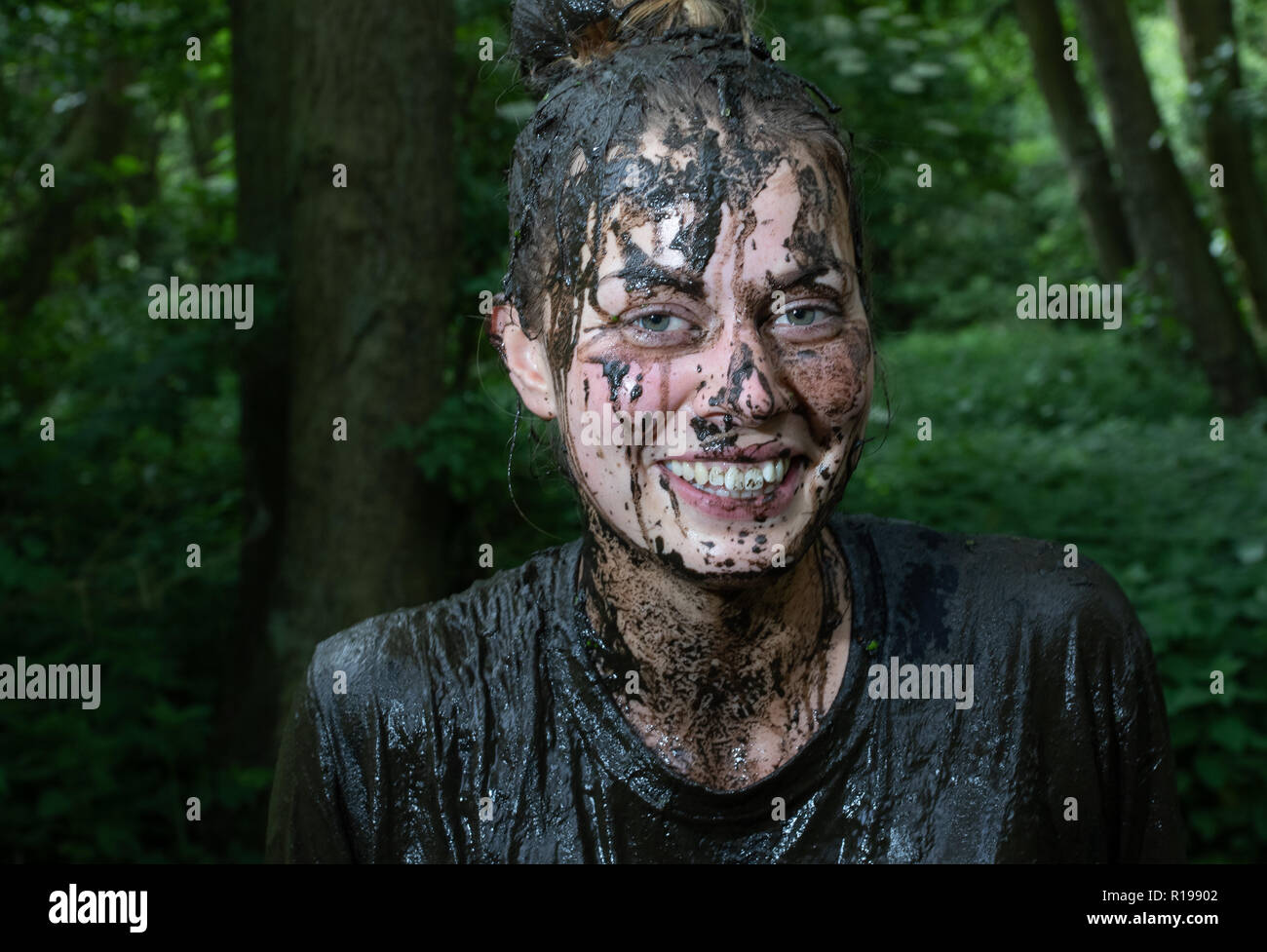 Smiling young woman covered in mud, even her teeth Stock Photo