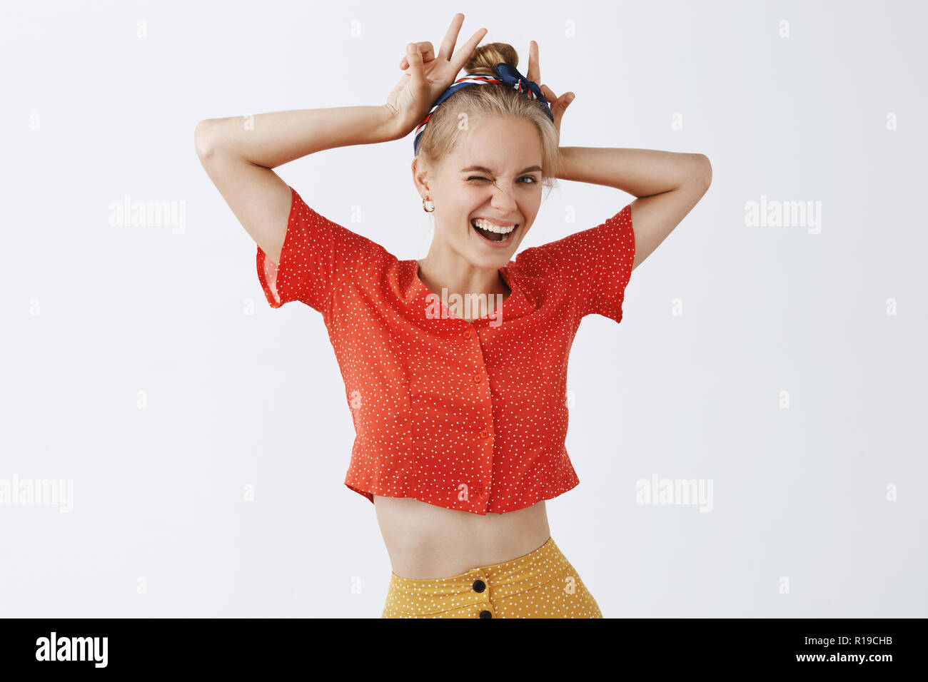 Try ruin my mood, you will fail. Portrait of joyful rebellious and cute female with fair hair in headband and dotted blouse showing peace or v-sign as Stock Photo