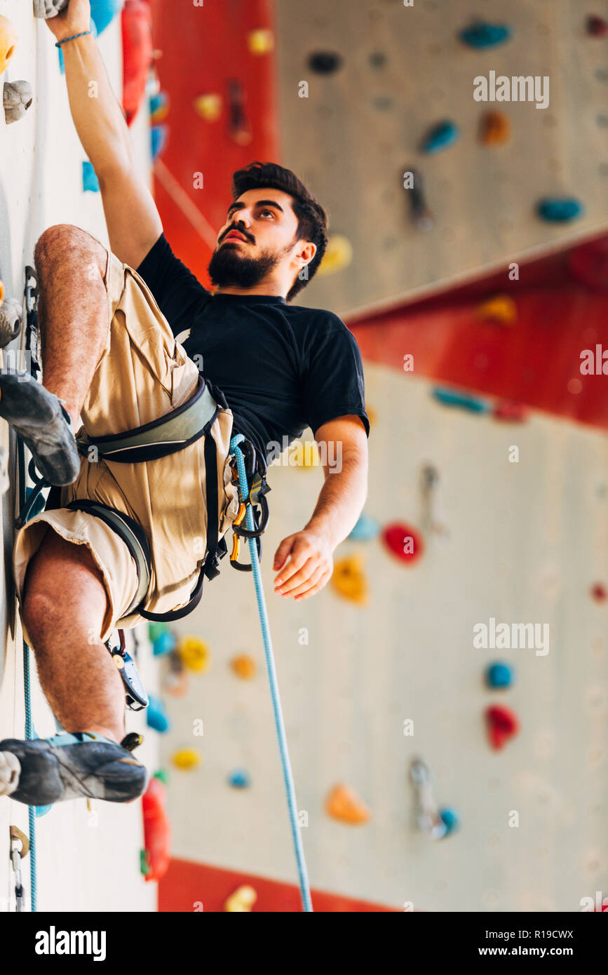 Man wearing belaying rope, climbing on a very high rock climbing wall ...