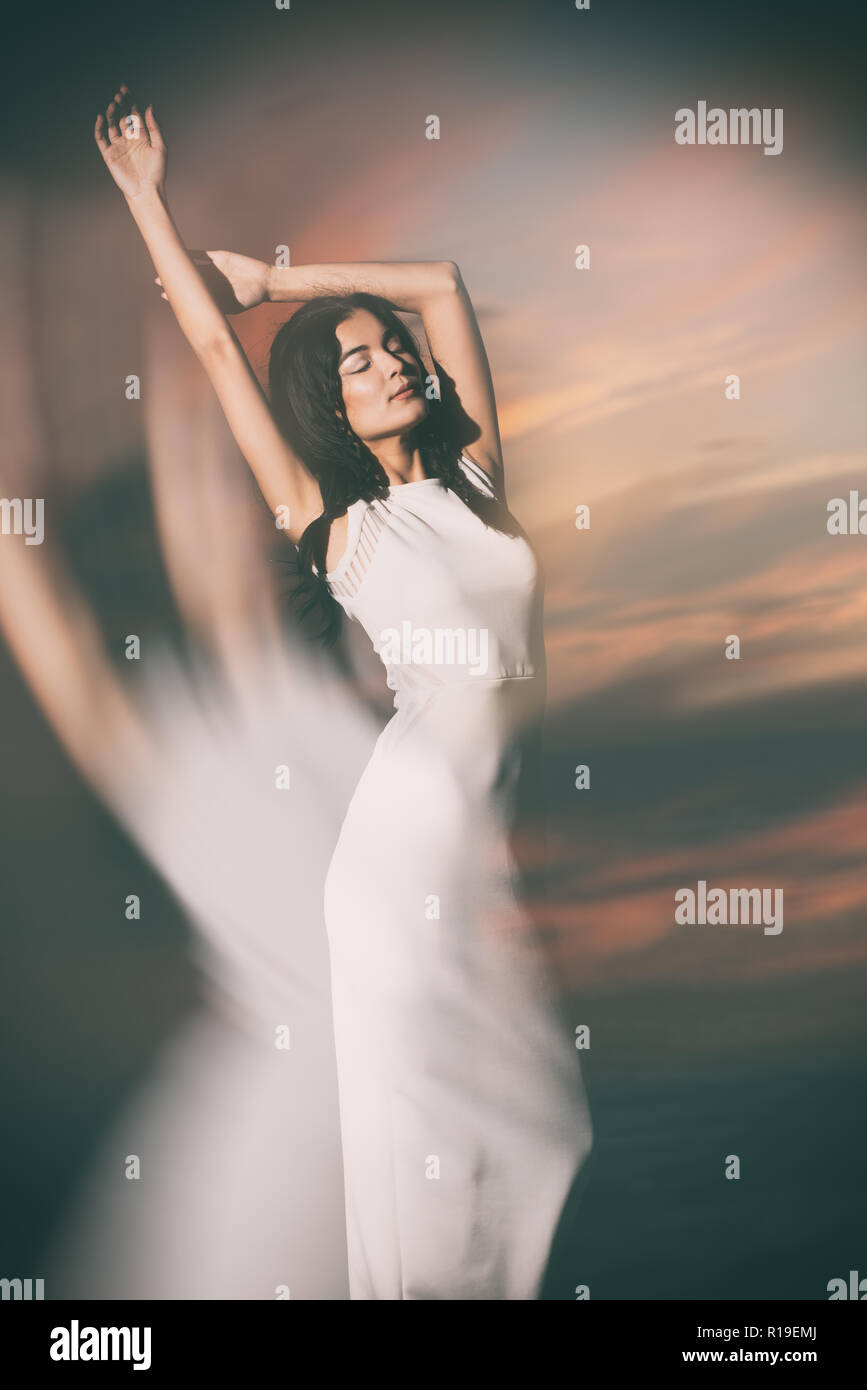 A beautiful female model, Asian, Mixed race model, modeling a simple white dress, a fashion editorial outdoor lifestyle concept against a dark sky. Stock Photo