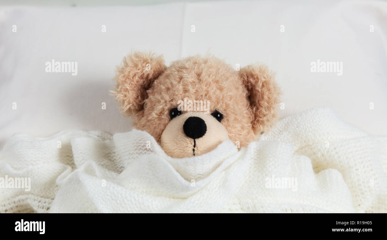 Kids bedtime. Cute teddy covered with a warm blanket, resting in bed Stock Photo