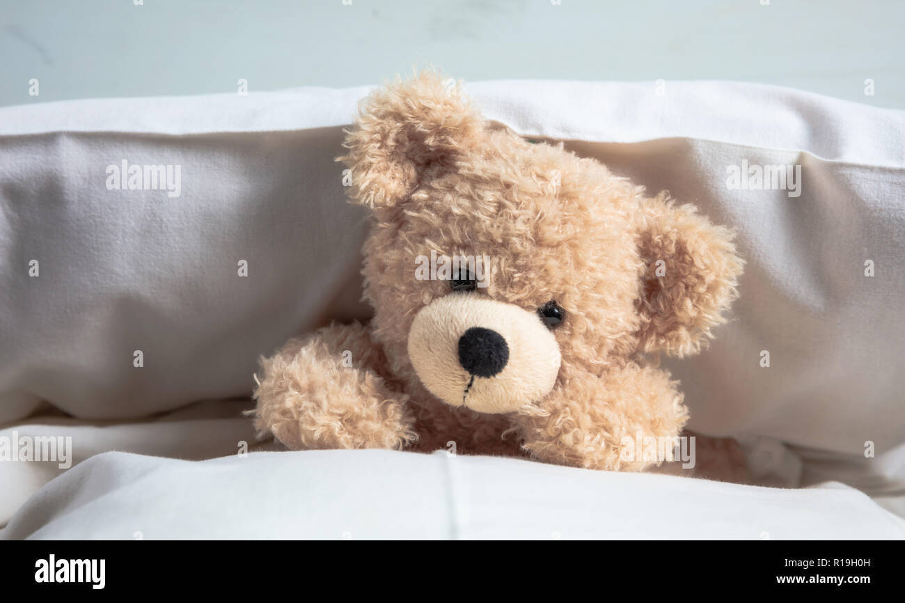 Kids bedtime. Cute teddy laying on bed mattress playing with pillows Stock Photo