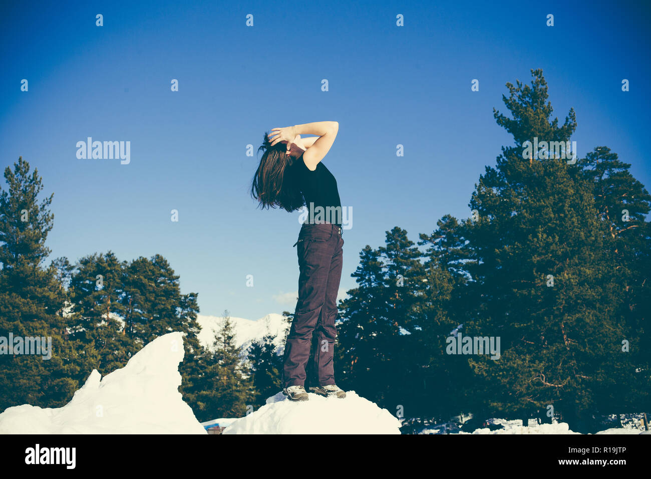 A young happy girl is standing in the snow and enjoying the sunshine. The concept of health and sports lifestyle Stock Photo