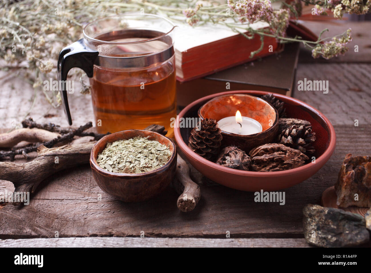 Healthy tea in glass teapot, dry herbs, plants and stones on wooden table. Homeopathy, alternative, occult ritual and herbal medicine concept, monochr Stock Photo