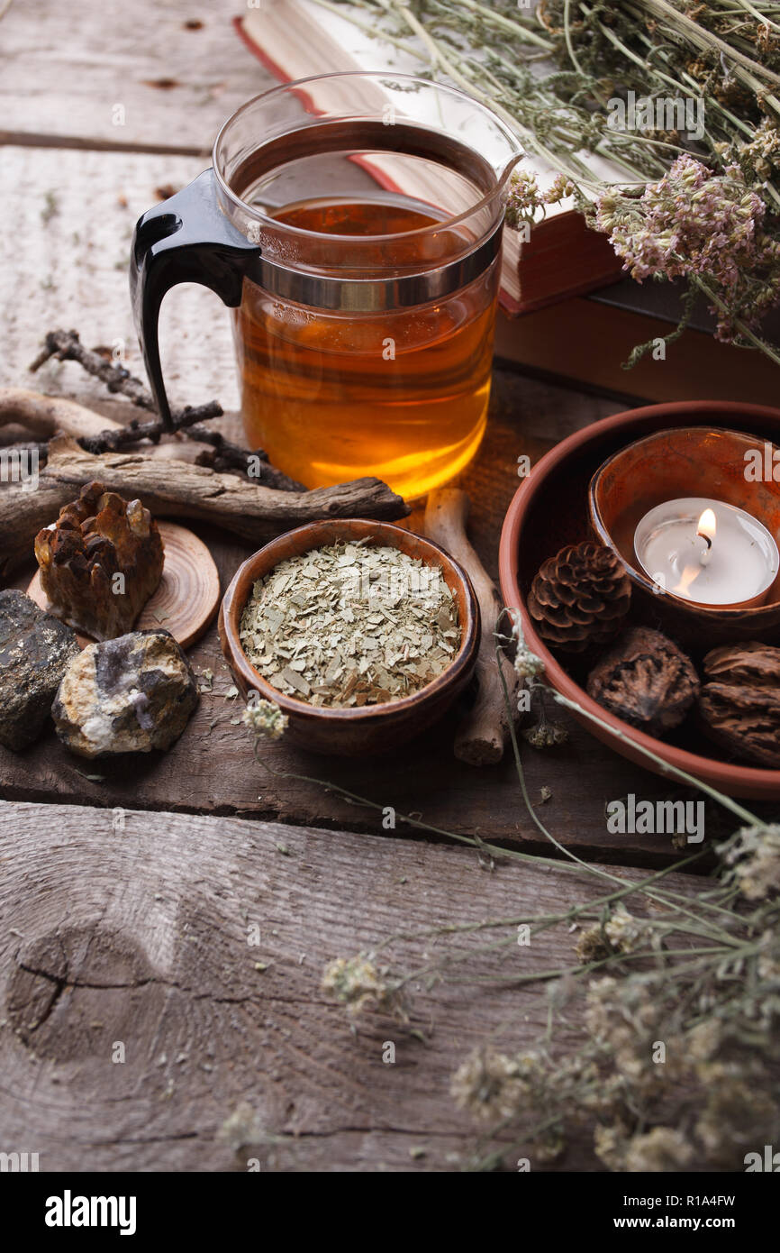Healthy tea in glass teapot, dry herbs, plants and stones on wooden table. Homeopathy, alternative, occult ritual and herbal medicine concept, monochr Stock Photo