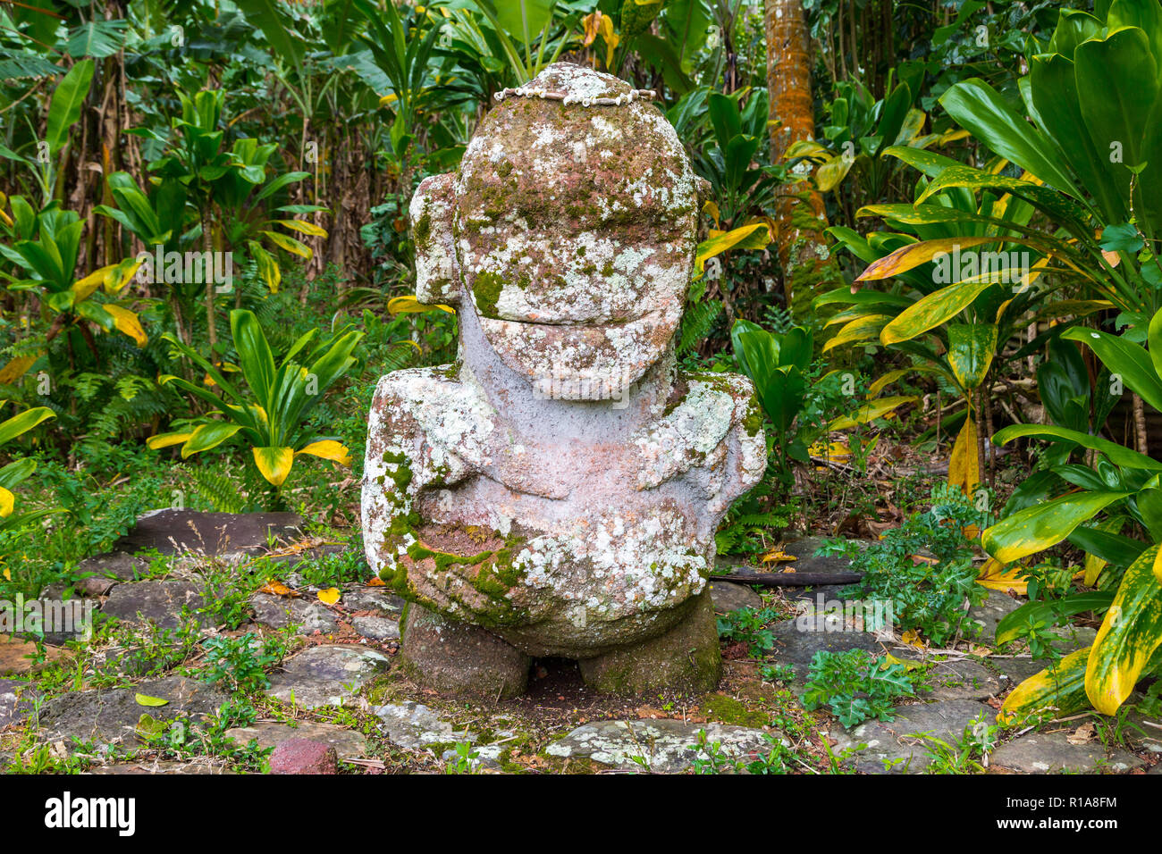 Smiling tiki. Carved stone tiki - Polynesian sacred idol statue hidden in jungle. Raivavae island, Astral islands (Tubuai), French Polynesia, Oceania Stock Photo