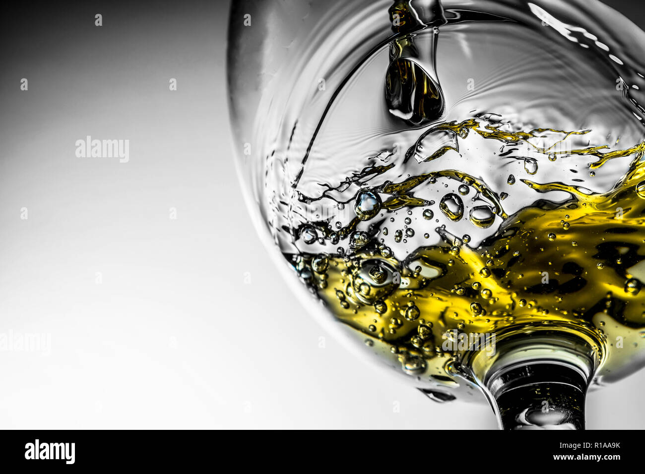 Stream of white wine pouring into a glass, white wine splash close-up on a grey background. Black and white photo with color of wine. Stock Photo