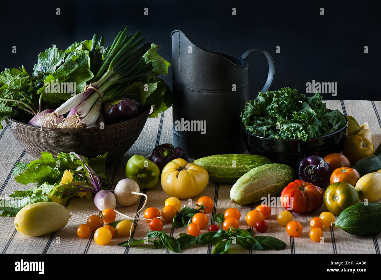 A still life scene of a bounty of fresh produce including tomatoes, turnips, kale, peppers, and cucumbers. Stock Photo