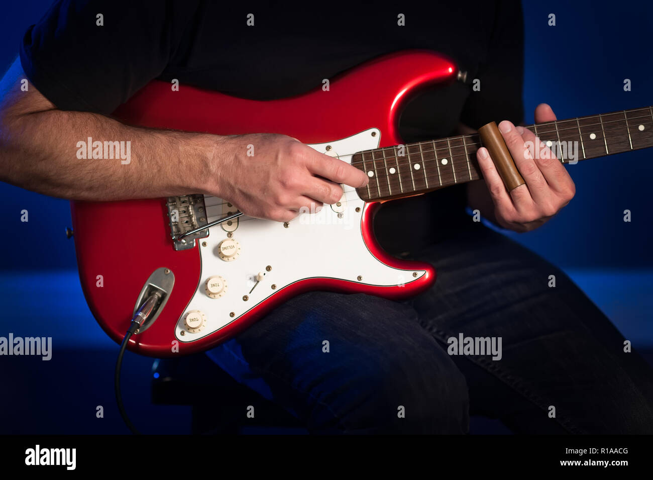 A close up view of a man playing a red and white electric guitar. Stock Photo