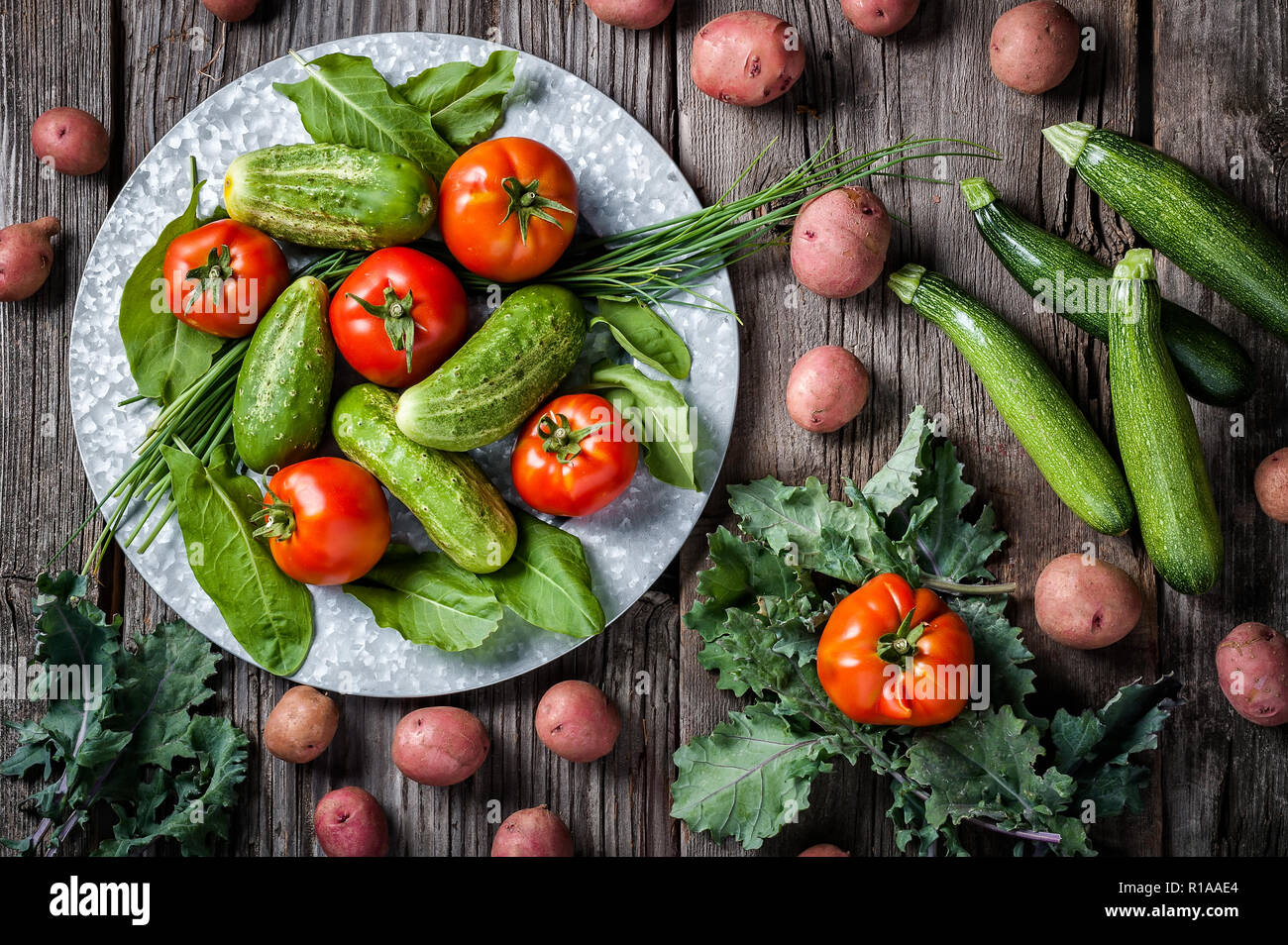 A produce scene of freshly harvested cucumber, tomatoes, red potatoes, kale, zucchini squash and kale on a rustic background. Stock Photo