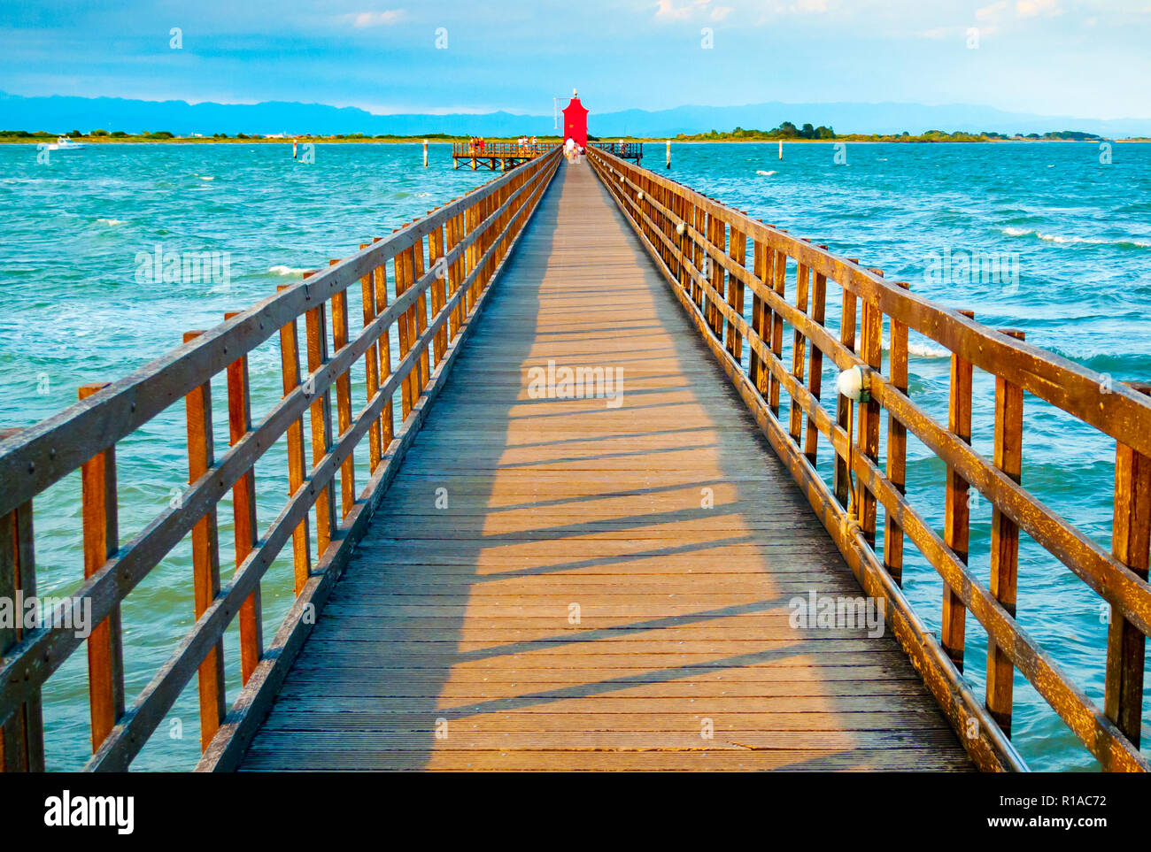 Wooden pier leading to a red lighthouse at sunset in Lignano Sabbiadoro, Friuli, Italy Stock Photo