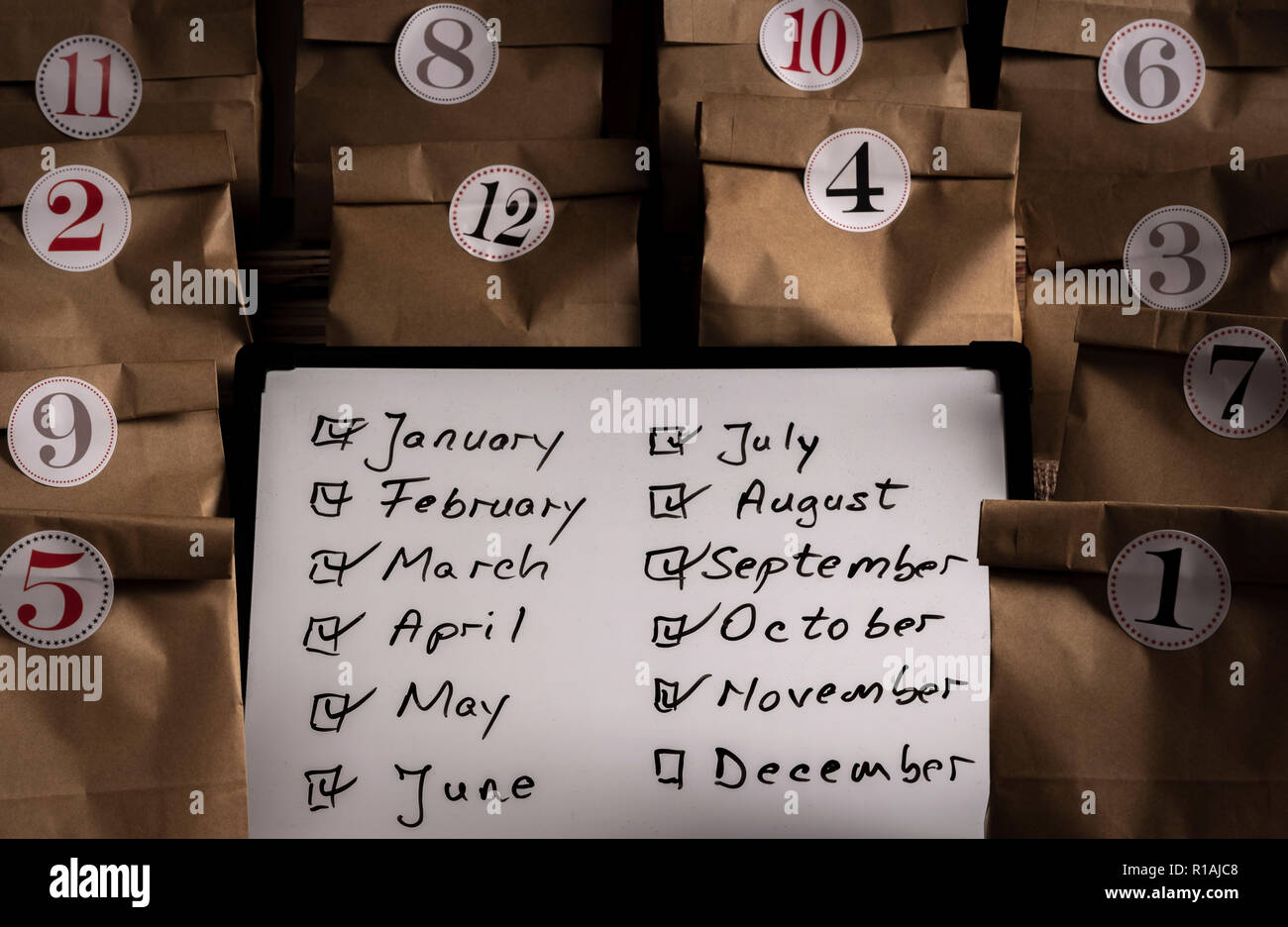 Writing board with the list of the months of the year and paper bags numbered from 1 to 12 with stickers. Traditional advent calendar gifting in small Stock Photo