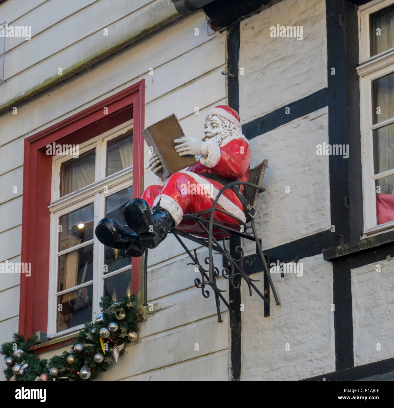 A model of Father Christmas sitting on a chair reading a book, which is ...