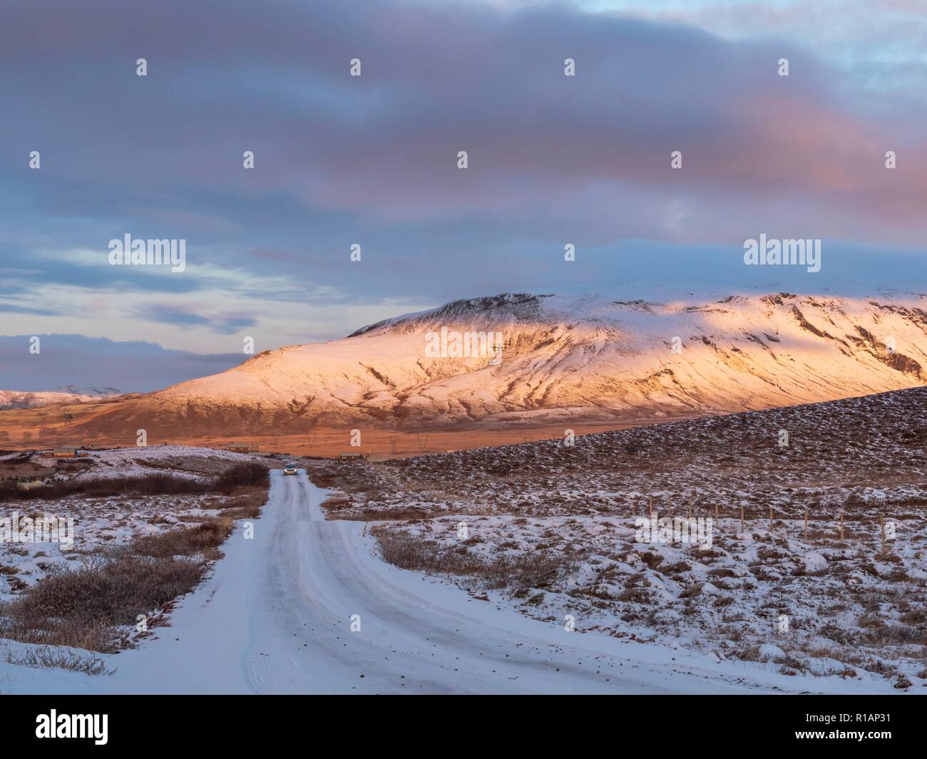A snow covered road leading towards a sunlit mountain in Iceland Stock Photo